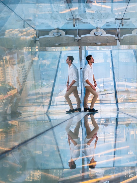 Man walking on glass slide at Sky Views Observatory with cityscape below.