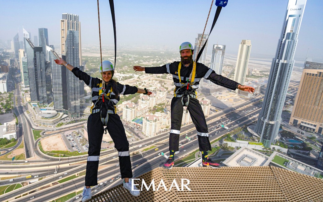 Participants on Edge Walk at Sky Views Observatory, Dubai, with city skyline in background.