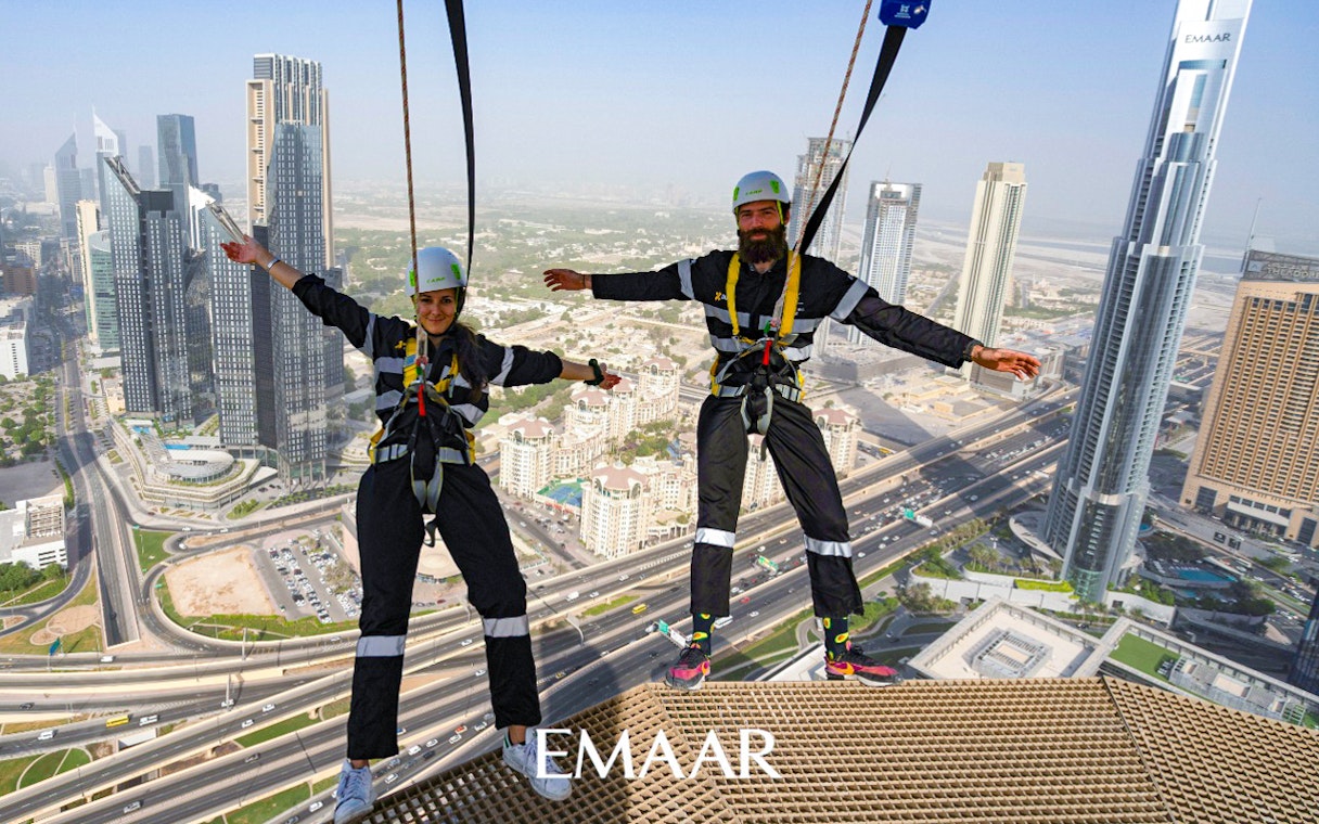 Participants on Edge Walk at Sky Views Observatory, Dubai, with city skyline in background.