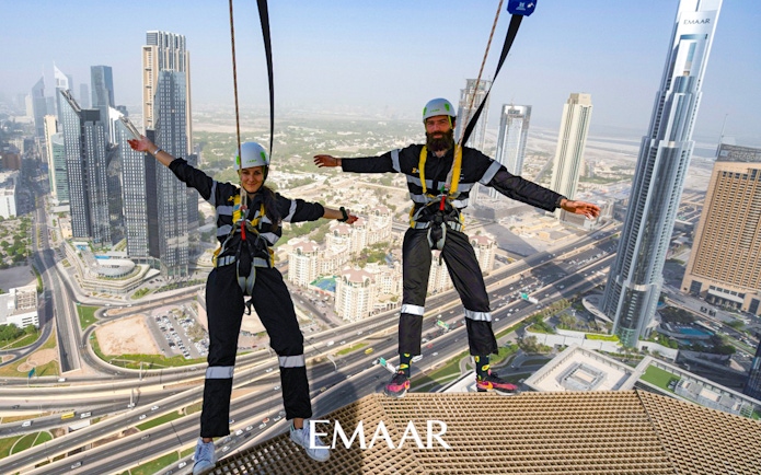 Participants on Edge Walk at Sky Views Observatory, Dubai, with city skyline in background.