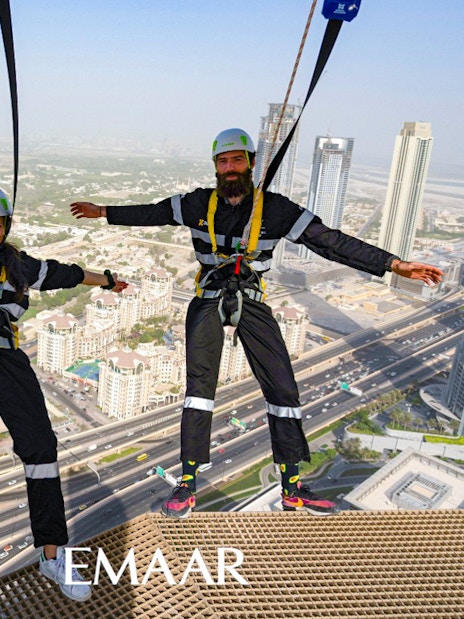 Participants on Edge Walk at Sky Views Observatory, Dubai, with city skyline in background.