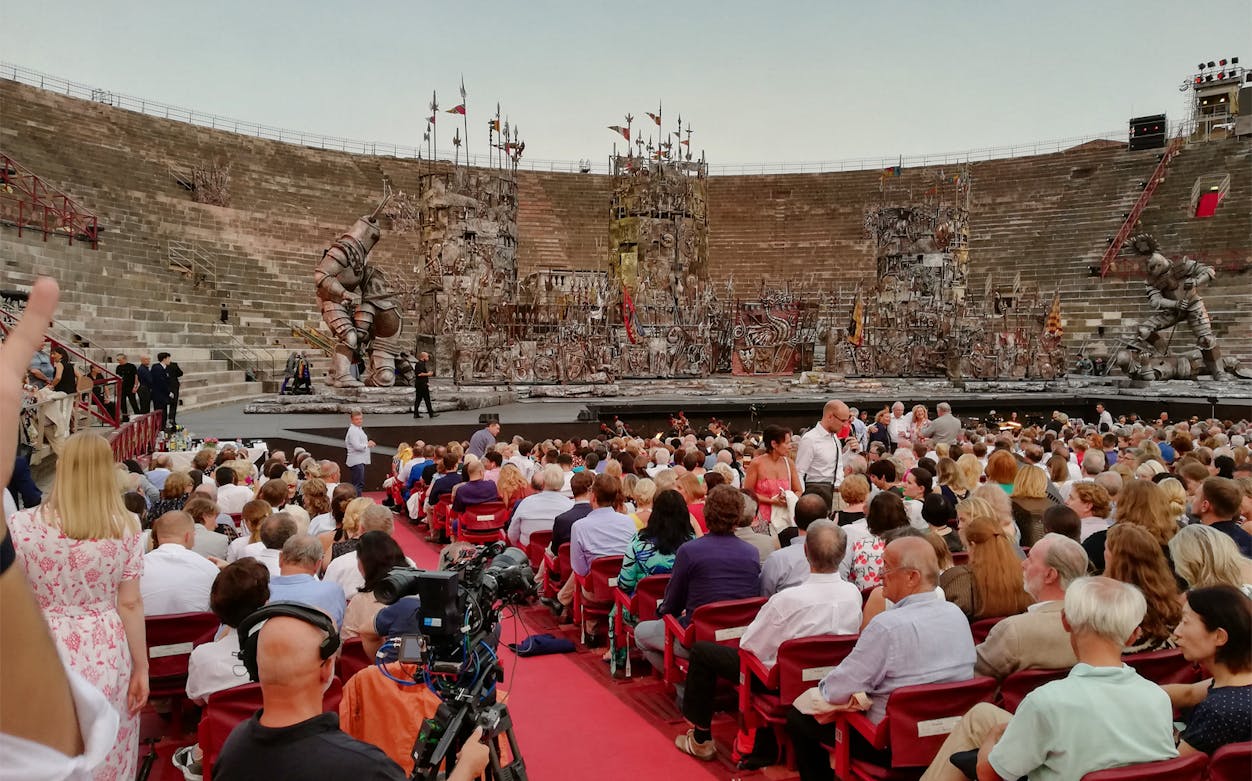 Crowd seated at Arena di Verona for an opera performance with elaborate stage set.