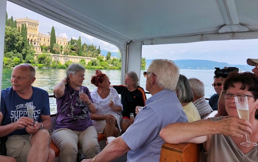 Boat cruise on Lake Garda with view of Isola del Garda villa, group enjoying drinks.