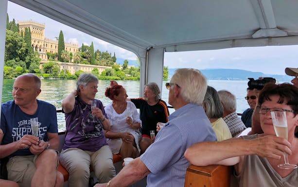Boat cruise on Lake Garda with view of Isola del Garda villa, group enjoying drinks.