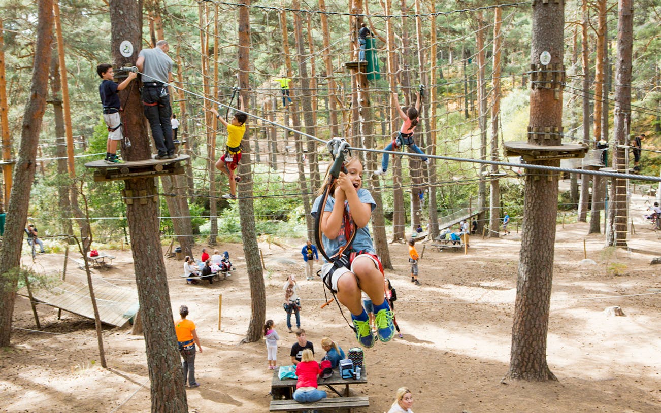 Children zip-lining and climbing at Aventura Amazonia in Pelayos forest adventure park.
