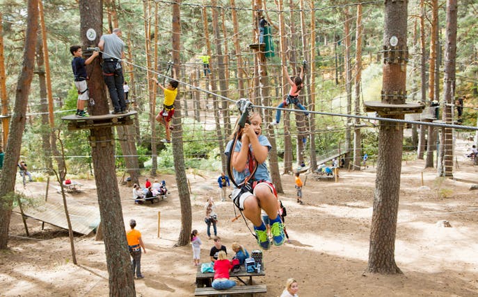 Children zip-lining and climbing at Aventura Amazonia in Pelayos forest adventure park.