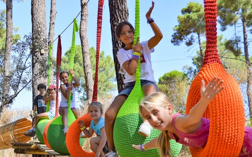 Children playing on colorful swings at Aventura Amazonia, Pelayos forest adventure park.