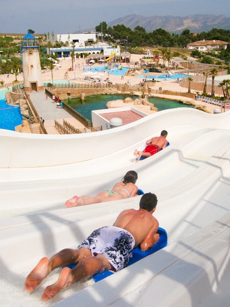 Visitors sliding down water slides at Terra Natura Benidorm with pools and landscape in view.