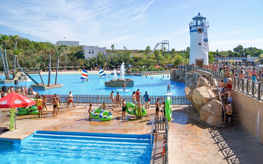 Visitors enjoying the water park at Terra Natura Benidorm with a lighthouse and pool activities.