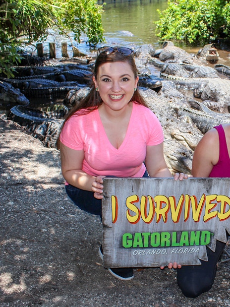 Visitors holding "I Survived" sign with alligators in Gatorland, Orlando.