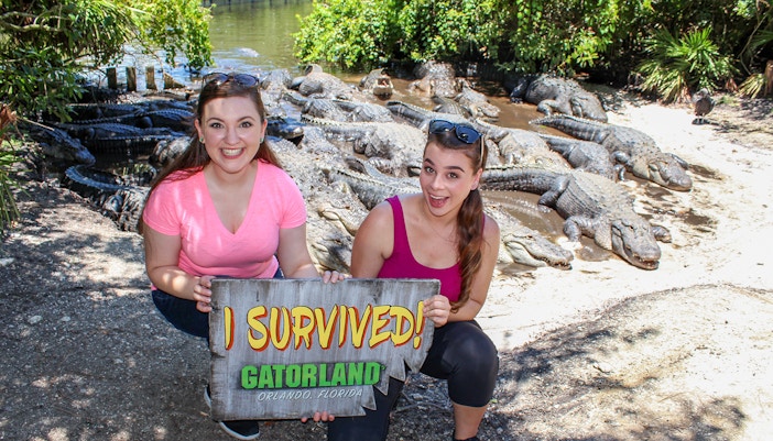 Visitors holding "I Survived" sign with alligators in Gatorland, Orlando.
