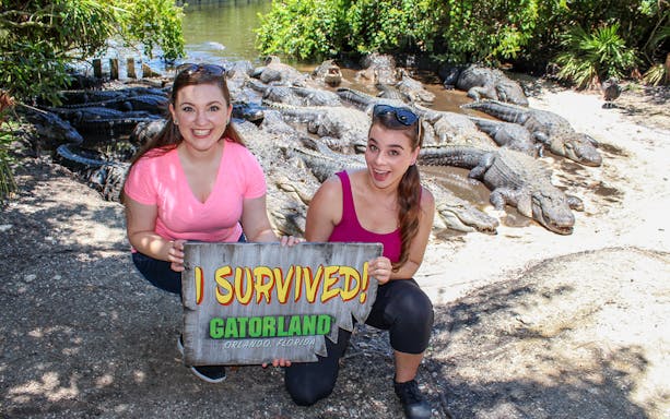 Visitors holding "I Survived" sign with alligators in Gatorland, Orlando.