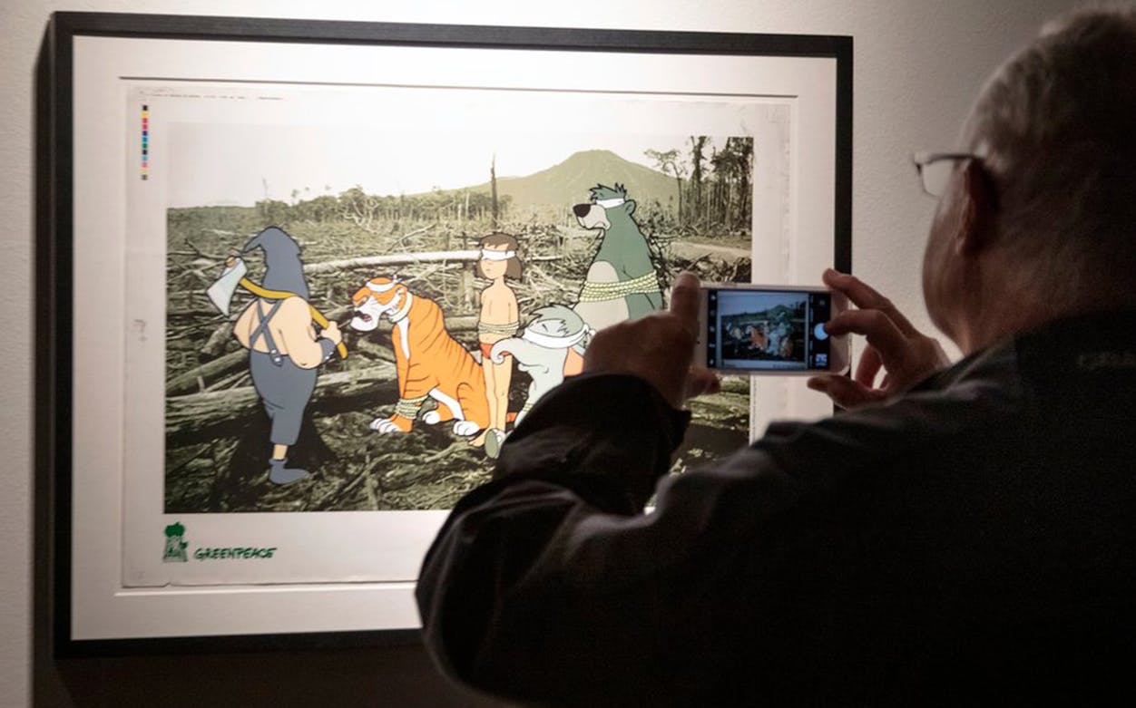 Banksy artwork at London exhibition featuring cartoon characters in a deforested landscape.