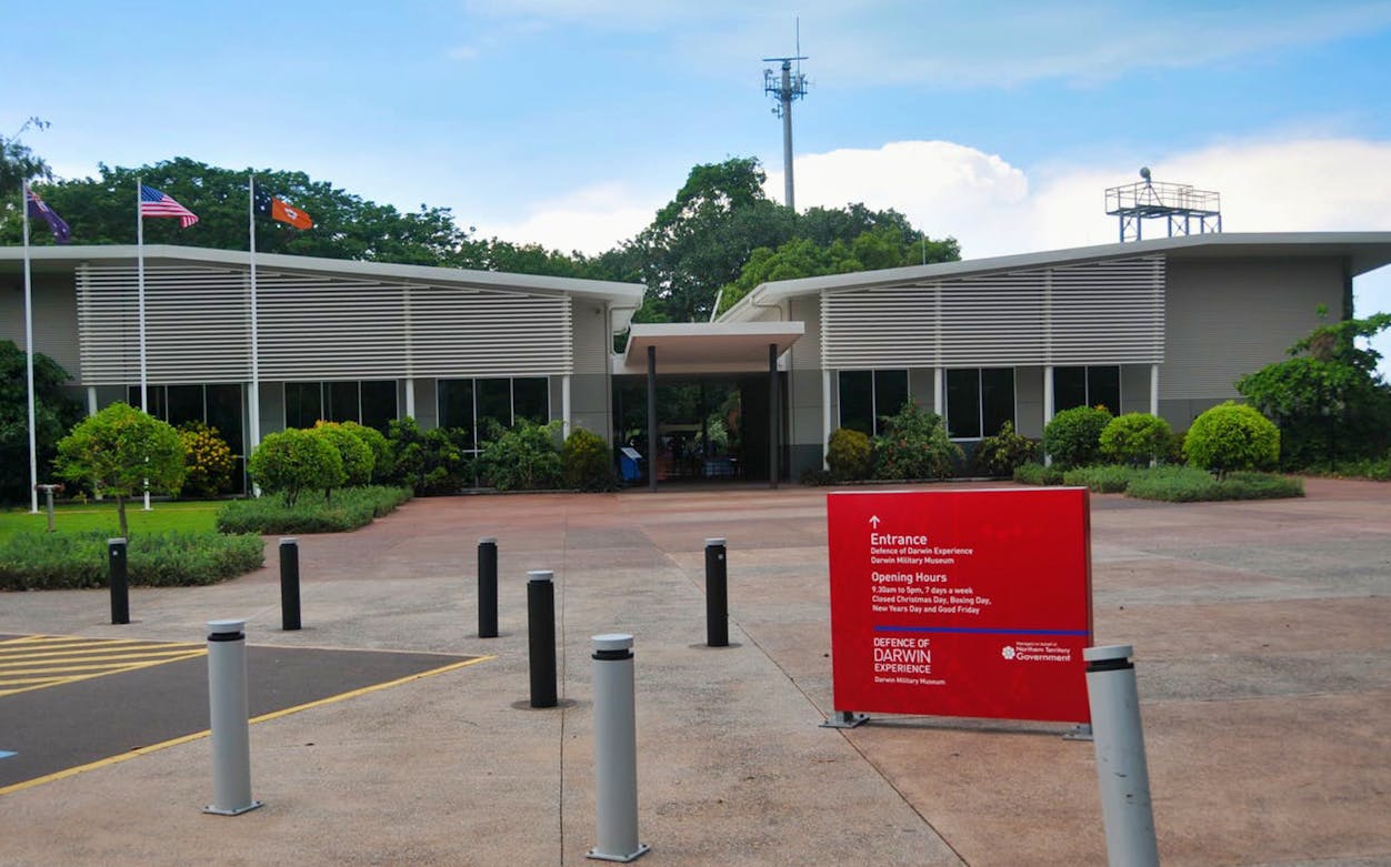 Darwin Military Museum entrance with flags and sign displaying opening hours.