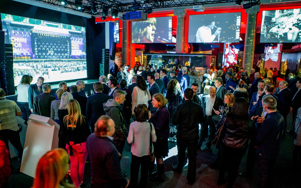 Crowd at The British Music Experience with concert footage on screens.