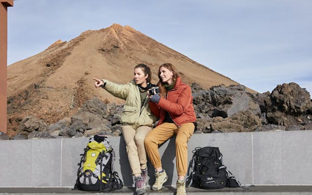 Two hikers with backpacks at Mount Teide, pointing towards Pico Viejo viewpoint.