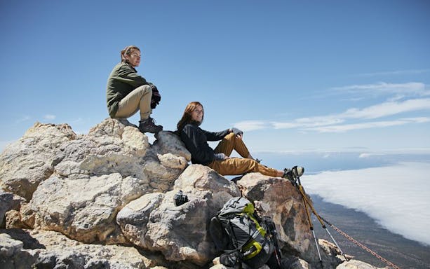Hikers resting on rocks at Teide Crater with view of clouds and landscape below.