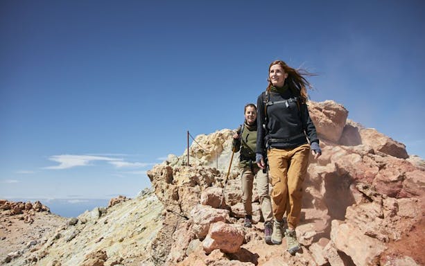 Hikers ascending rocky path on Teide Crater, Tenerife, with clear blue sky.