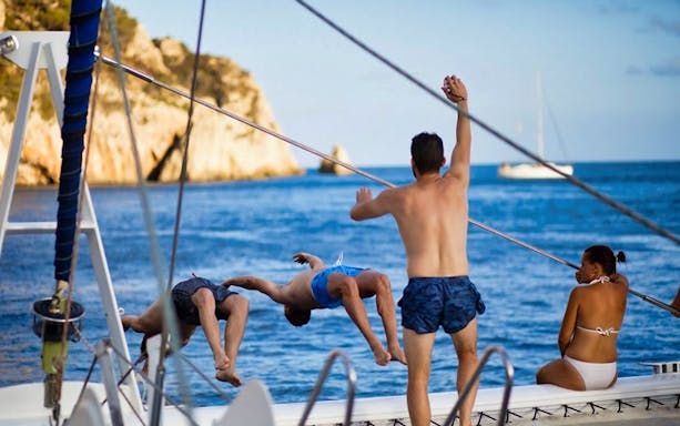 People enjoying a boat tour in Valencia, with two jumping into the sea and scenic cliffs in the background.