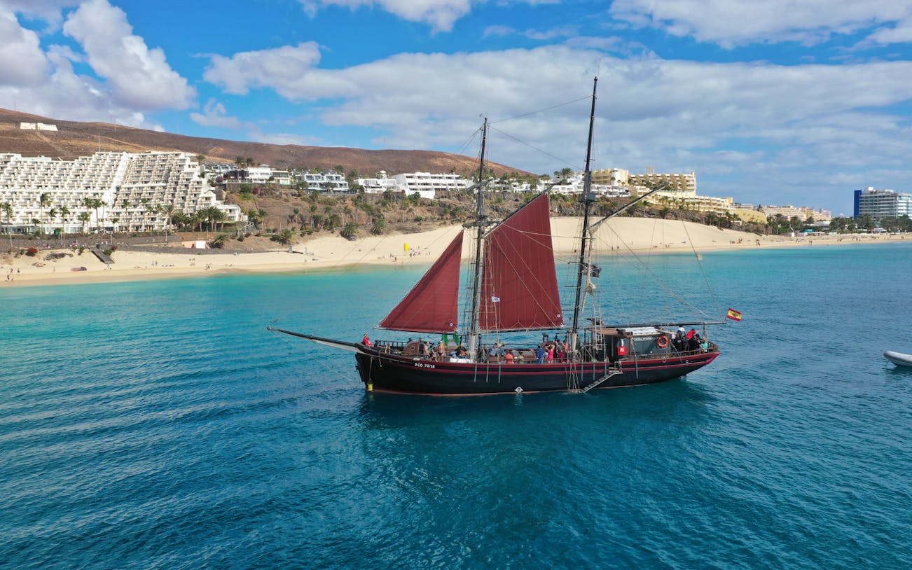 Pirate ship sailing near Fuerteventura beach with hotels in the background.