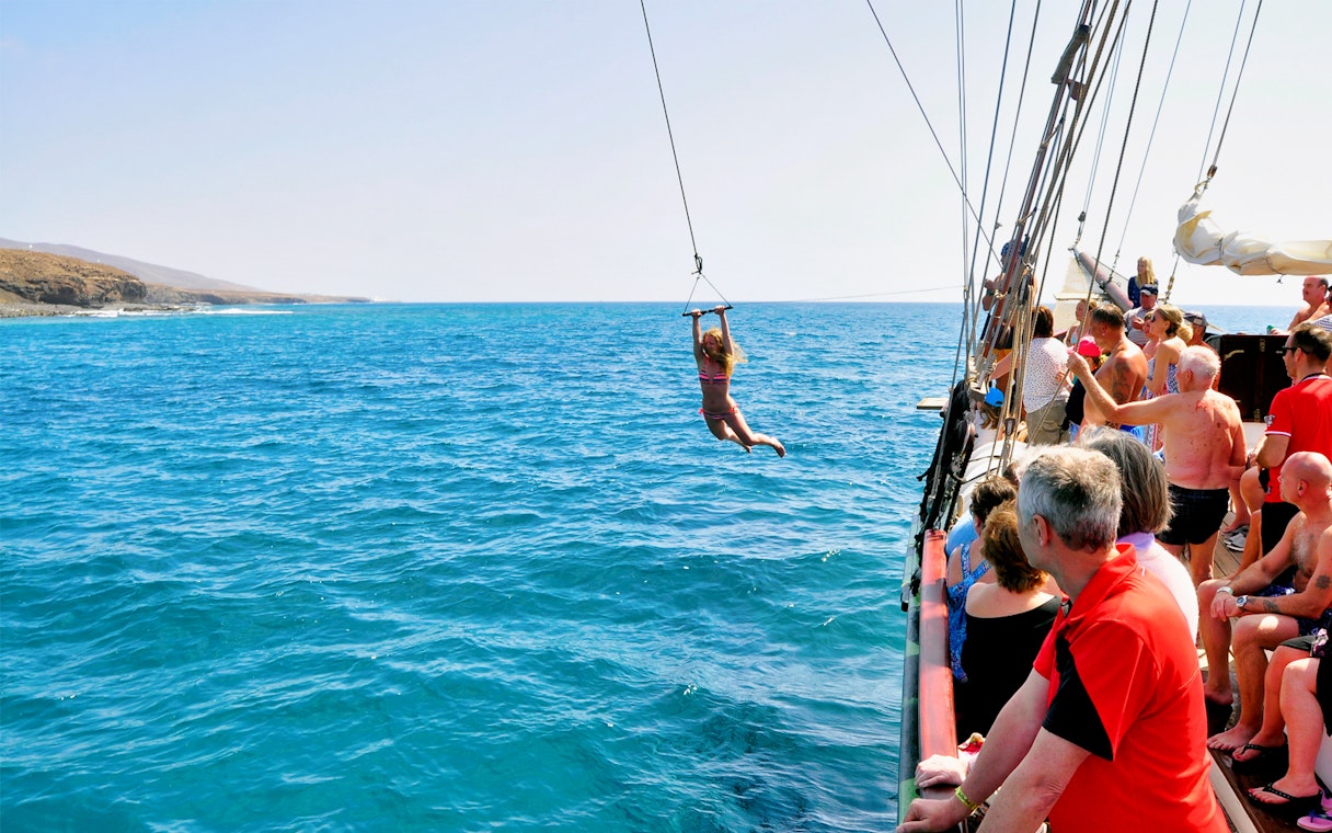 Pirate ship tour in Fuerteventura with a person swinging over the ocean.