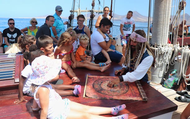 Children and adults on a pirate-themed boat tour in Fuerteventura, engaging with a costumed guide.