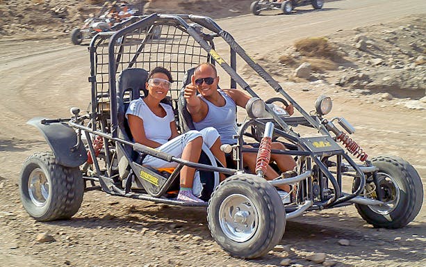 Two people riding a dune buggy on a dirt trail in Fuerteventura.