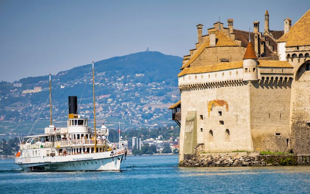 Steamboat cruising near Chillon Castle on Lake Geneva with Montreux hills in the background.