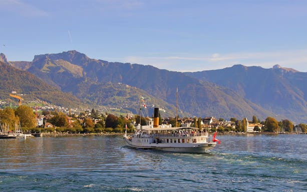 Cruise boat on Lake Geneva with Chillon Castle and Swiss Alps in the background.