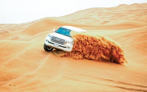SUV driving through sand dunes on a classic overnight desert safari.