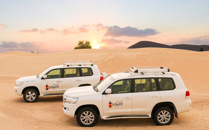 Two SUVs parked on desert sand during sunset, part of a classic overnight desert safari.