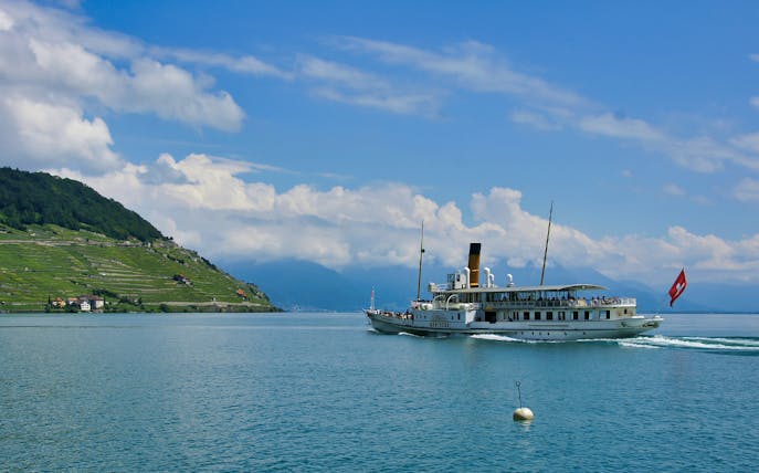 Cruise ship on Lake Geneva with Lavaux vineyards and Swiss flag in view.