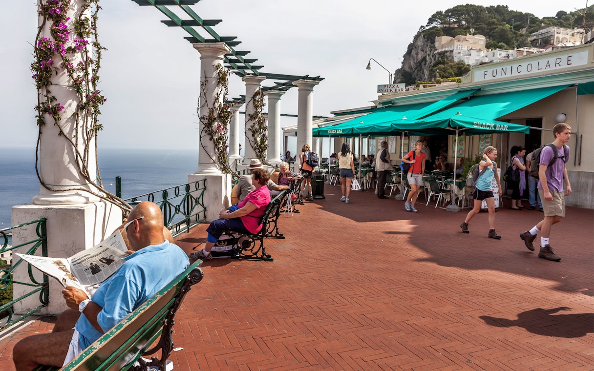 Capri promenade with people relaxing and walking near Funicolare, overlooking the sea.