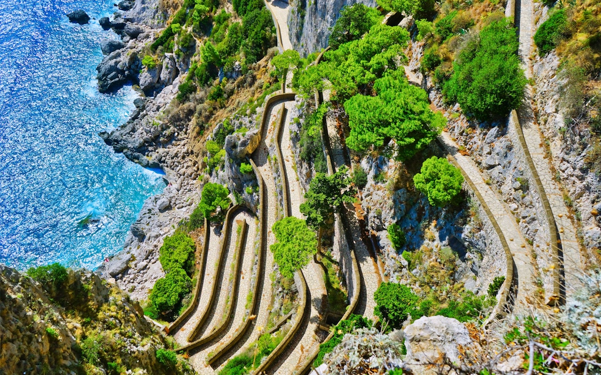 Winding path along rocky cliffs and greenery on Capri, Italy, seen from above.