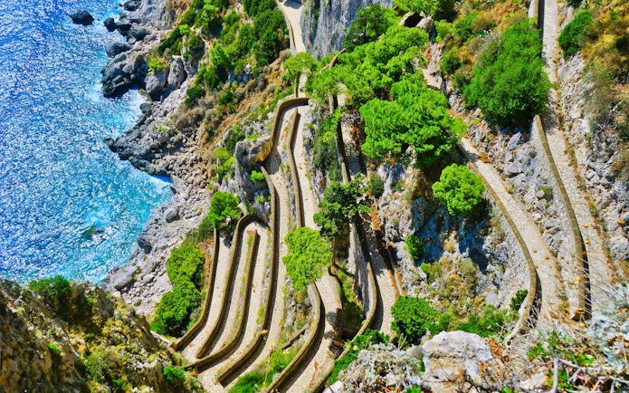 Winding path along rocky cliffs and greenery on Capri, Italy, seen from above.