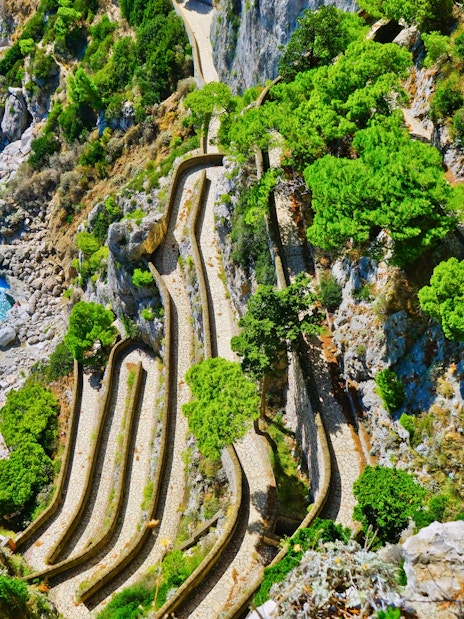 Winding path along rocky cliffs and greenery on Capri, Italy, seen from above.