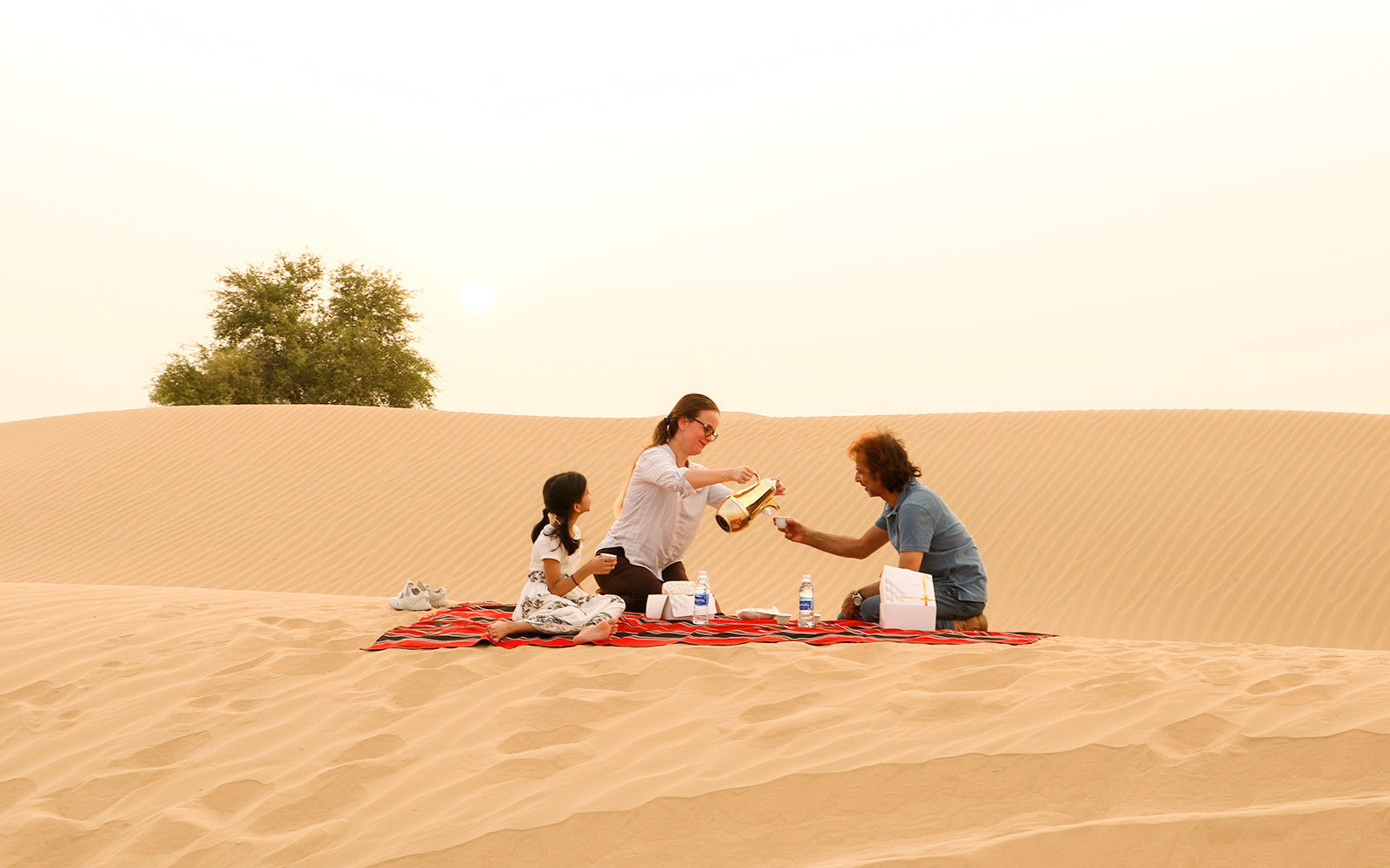 Family enjoying picnic on desert dunes during evening safari.