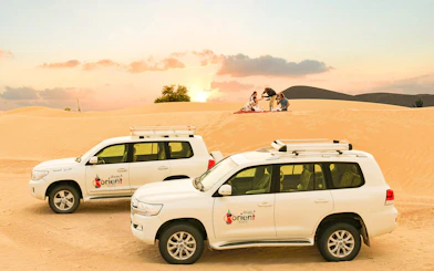Desert safari with SUVs and group enjoying picnic at sunset.