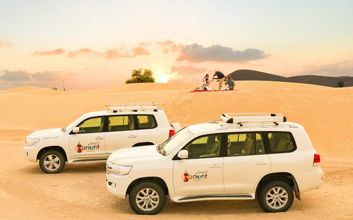 Desert safari with SUVs and group enjoying picnic at sunset.
