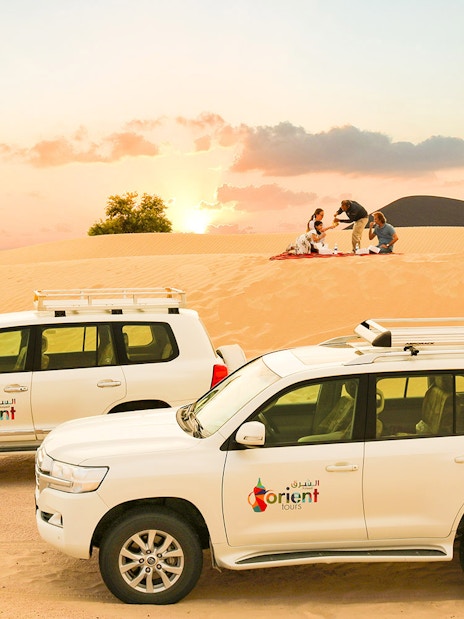 Desert safari with SUVs and group enjoying picnic at sunset.