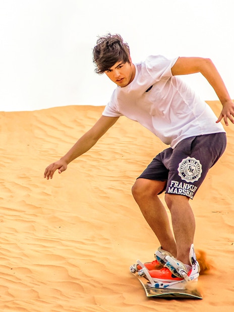 Sandboarding on desert dunes during evening safari experience.