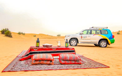Desert safari setup with cushions and lanterns, SUV in the background, UAE desert.