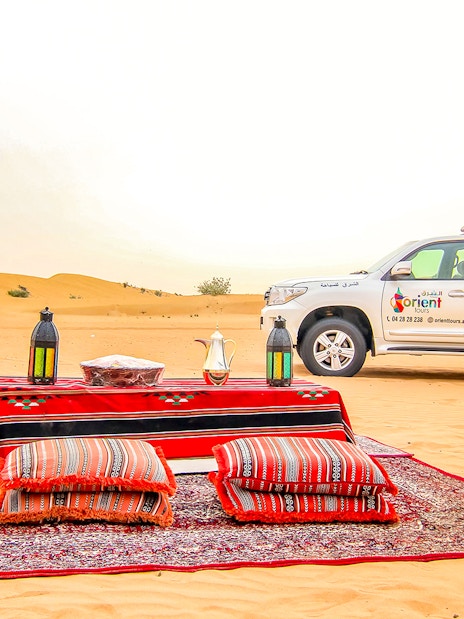 Desert safari setup with cushions and lanterns, SUV in the background, UAE desert.