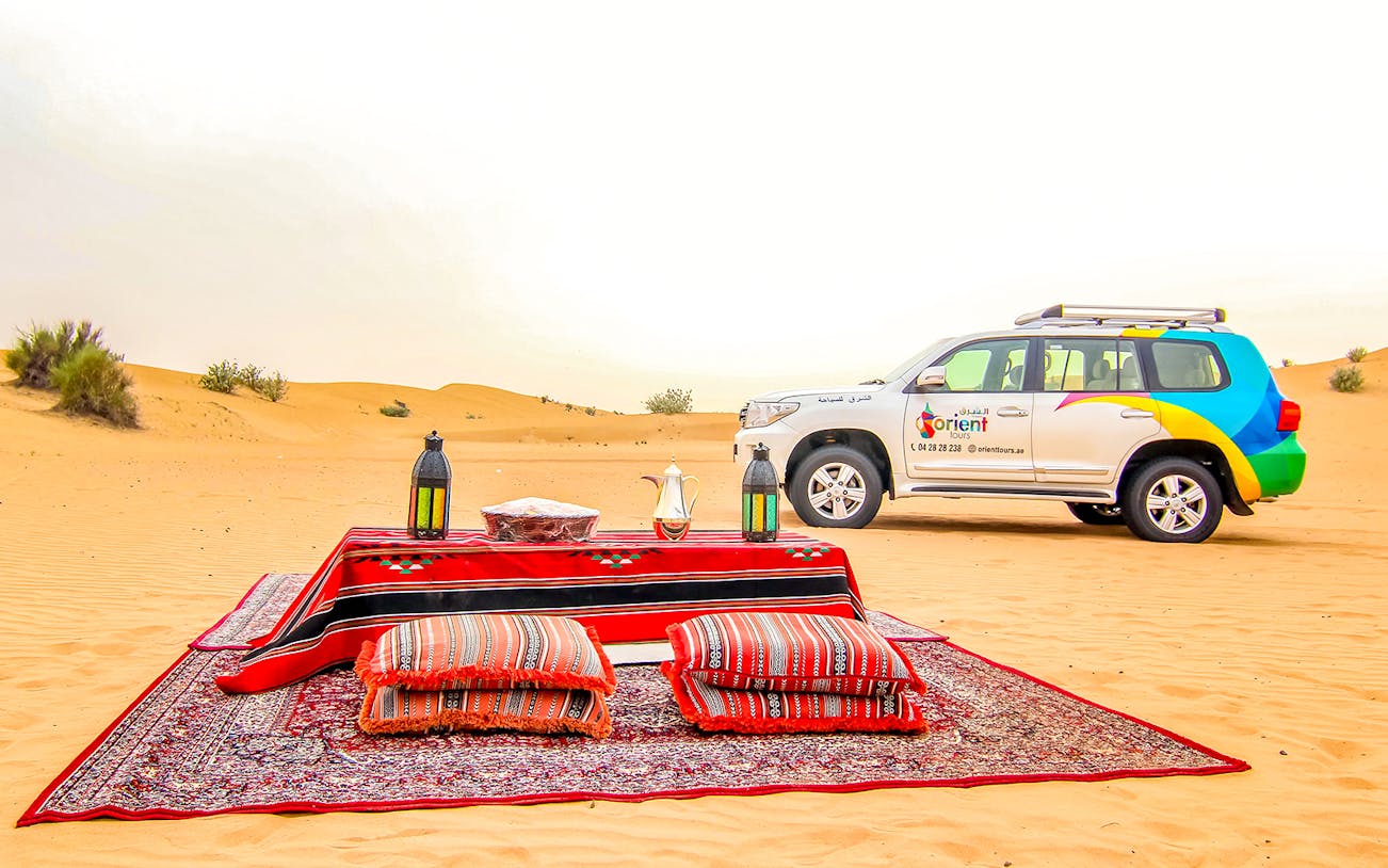 Desert safari setup with cushions and lanterns, SUV in the background, UAE desert.
