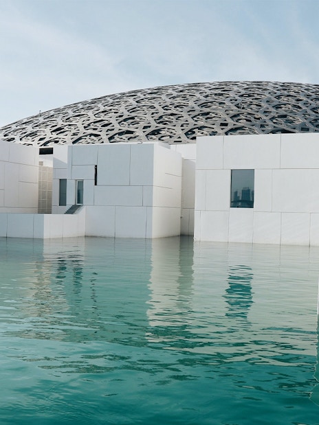 Louvre Abu Dhabi exterior with water reflection and dome structure.