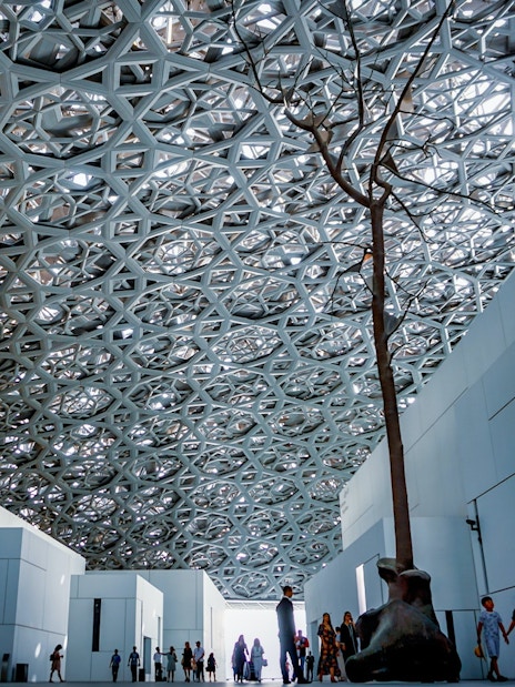 Louvre Abu Dhabi interior with geometric dome and visitors exploring exhibits.