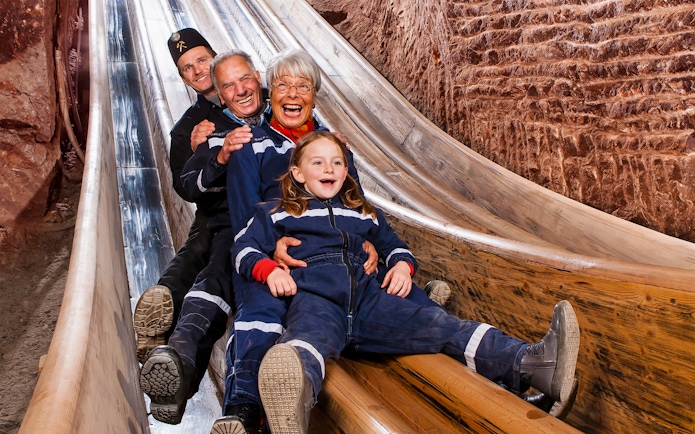Visitors sliding down wooden chute in Bavarian salt mine, Berchtesgaden tour from Salzburg.