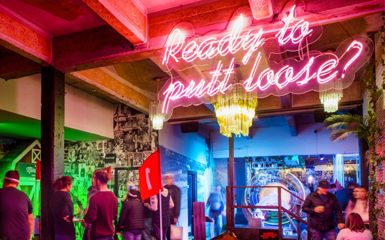 Holey Moley Golf Club interior with neon sign and people socializing.