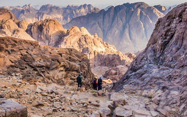 Hikers descending rocky path on Mount Moses at sunrise, Sinai Peninsula, Egypt.