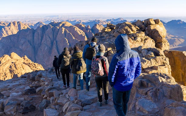 Hikers on a rocky trail in Sharm-El-Sheikh with mountain views in the background.
